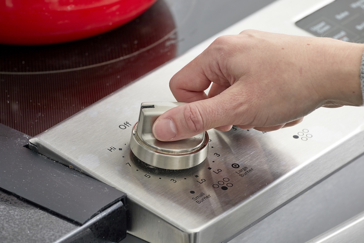 Woman turns dial on stovetop to high.