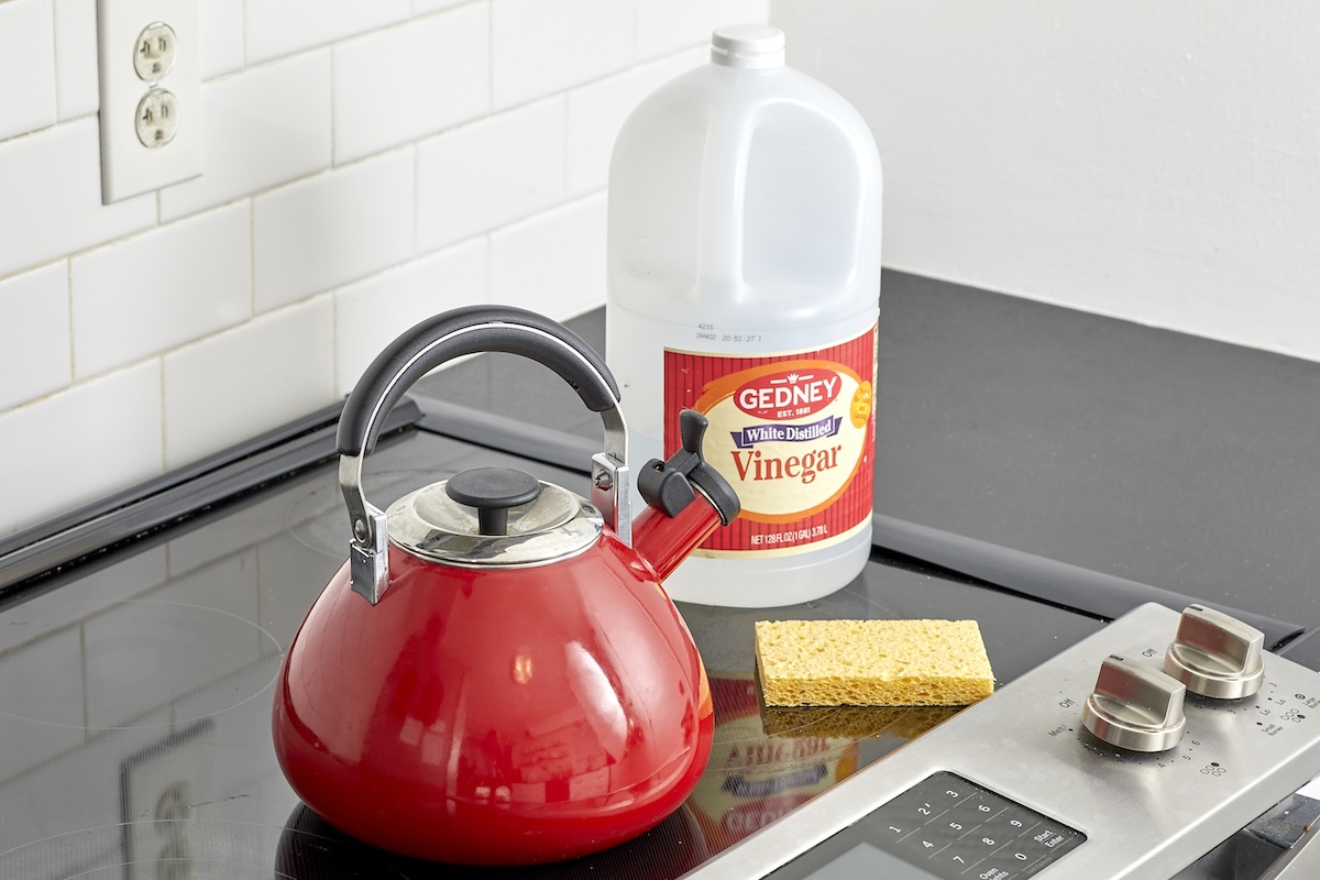 Red kettle, vinegar bottle, and sponge on a glass cooktop.