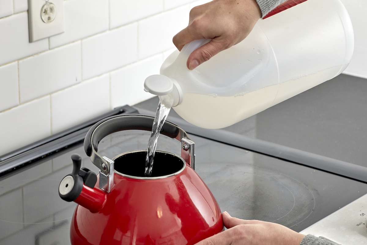 Woman pours vinegar from jug into a red kettle on a stovetop.