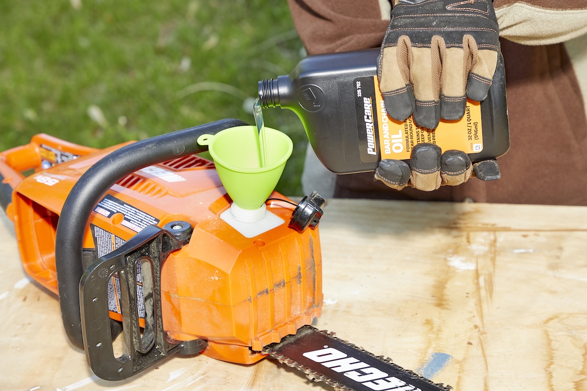 Person pours bar and chain oil into the chainsaw's reservoir.