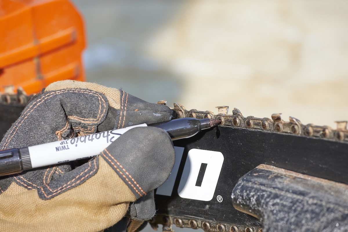 Person marks a cutter on a chainsaw with a permanent marker.