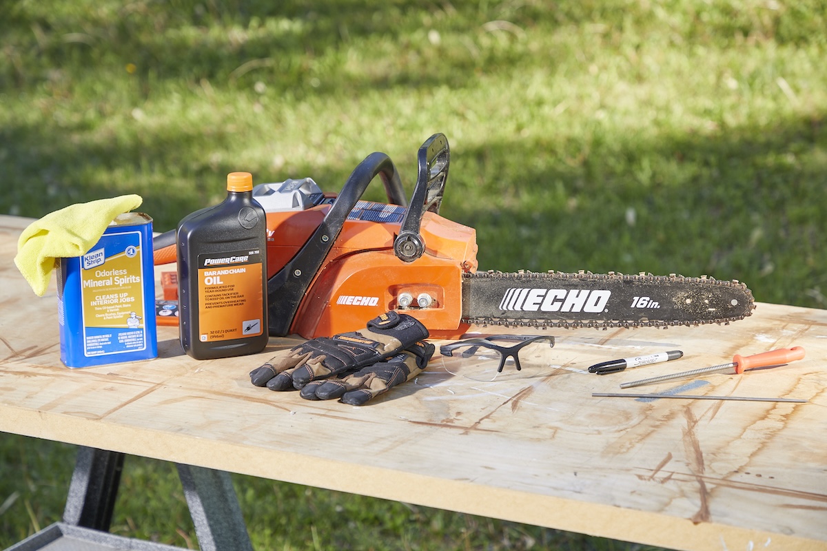 Chainsaw and materials needed to sharpen it on a wooden workbench outdoors.