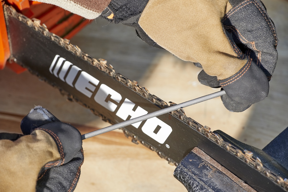 Person wearing work gloves files the teeth on a chainsaw chain.