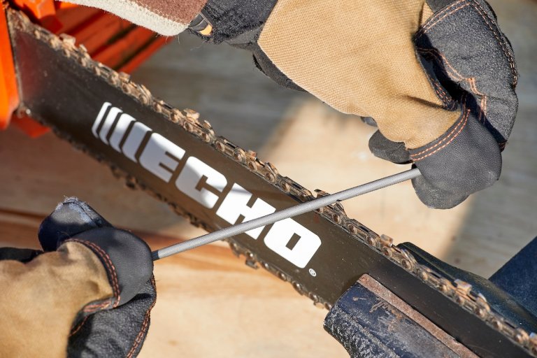 Person wearing work gloves files the teeth on a chainsaw chain.