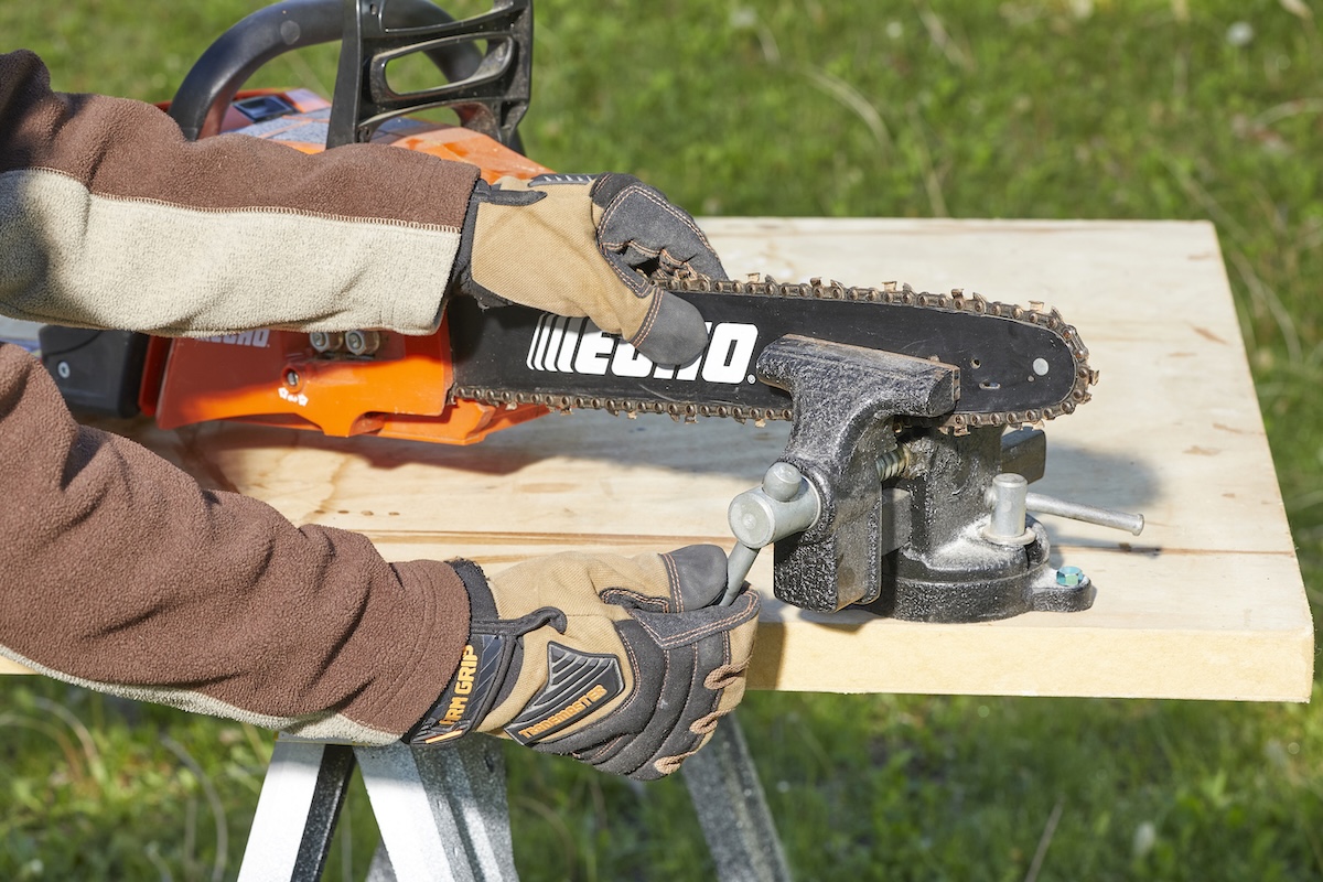 Woman stabilizes a chainsaw on a table using a clamp.