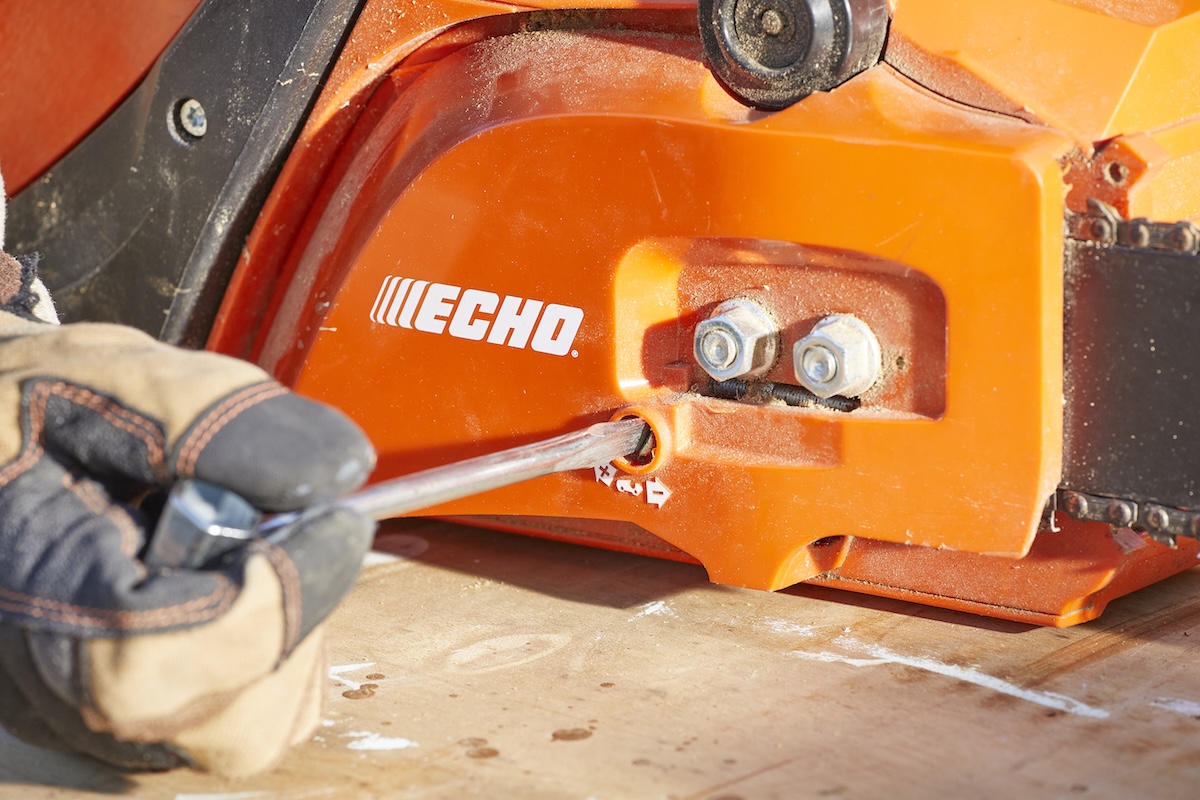 Person uses a screwdriver to adjust tension screw on an orange chainsaw.
