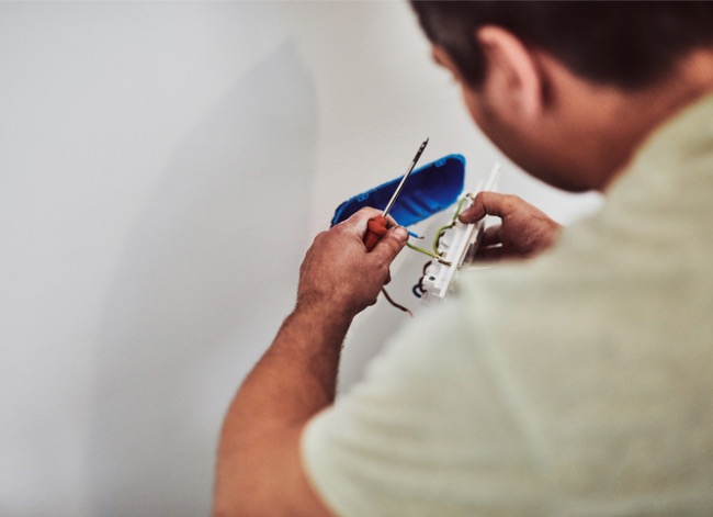 Man pulling electrical outlet out of an electrical outlet box.