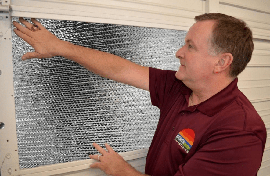 A man in a polo shirt installs garage door insulation between door panels on the inside of a garage.