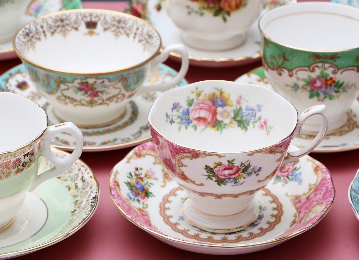 A collection of old-fashioned, floral painted teacups and saucers on a pink tablecloth.