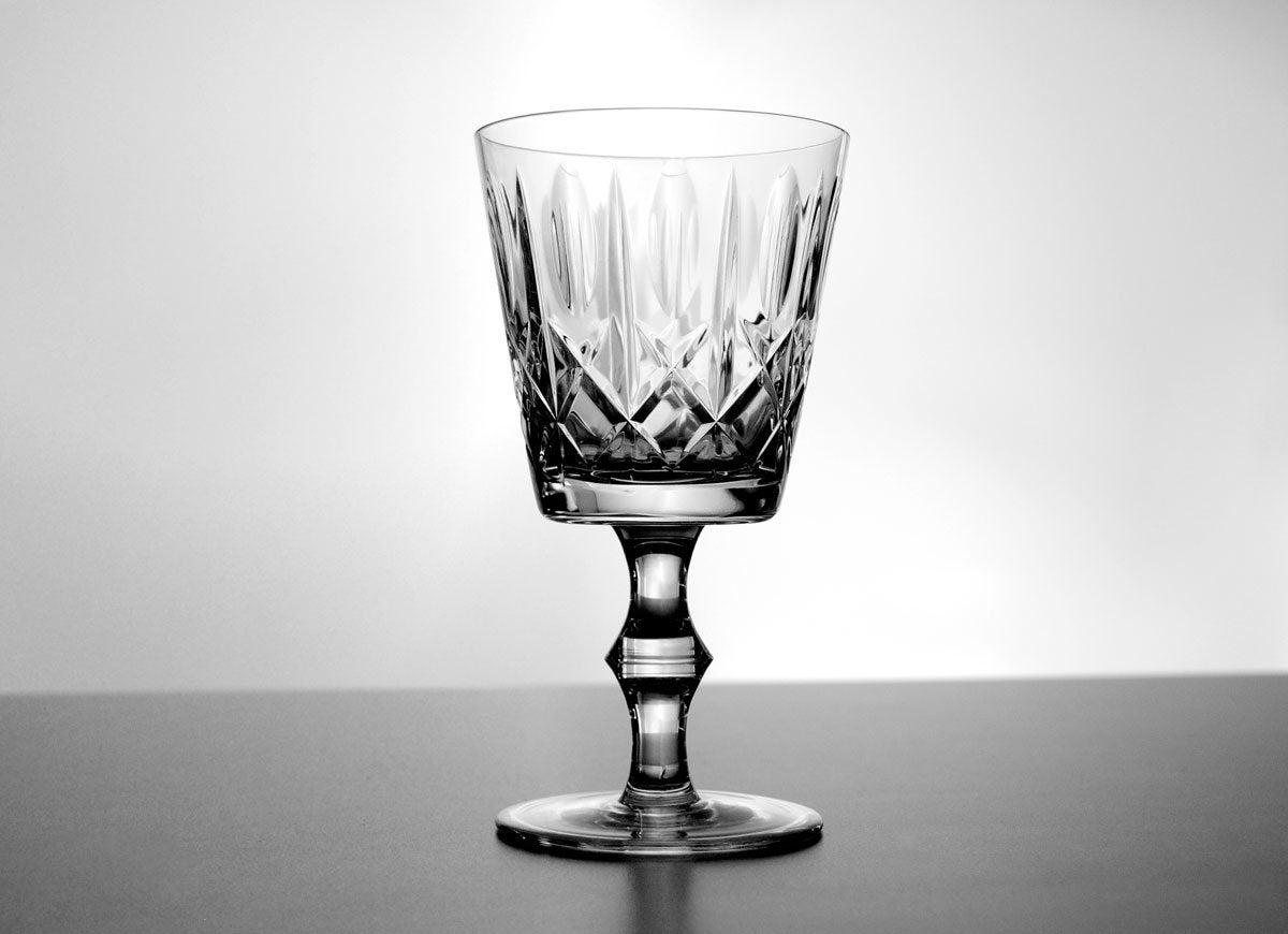 One cut crystal wine goblet on a grey surface.