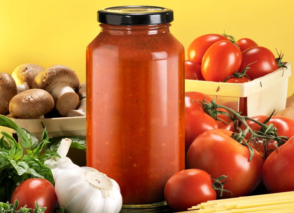 Jar without a label surrounded by tomatoes, mushrooms, garlic and basil.