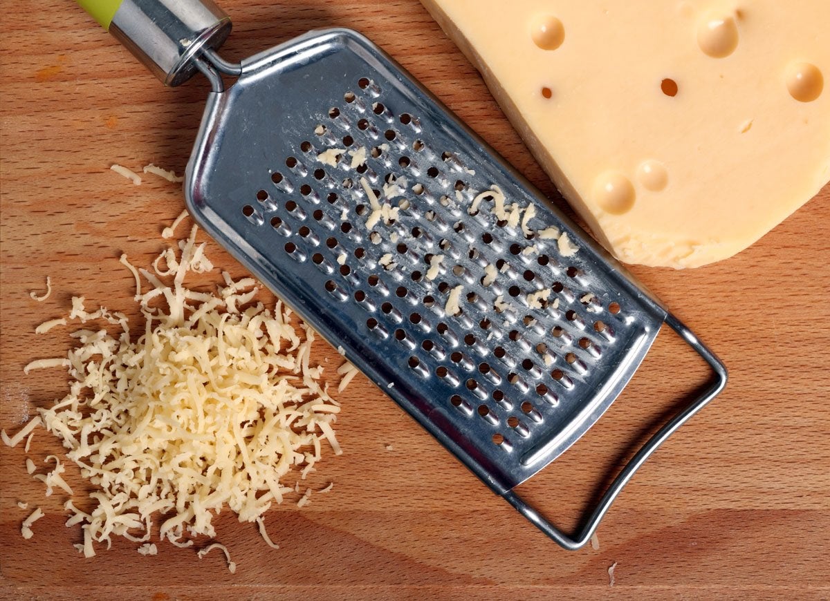 Cheese grater next to a block of Swiss cheese and grated cheese.