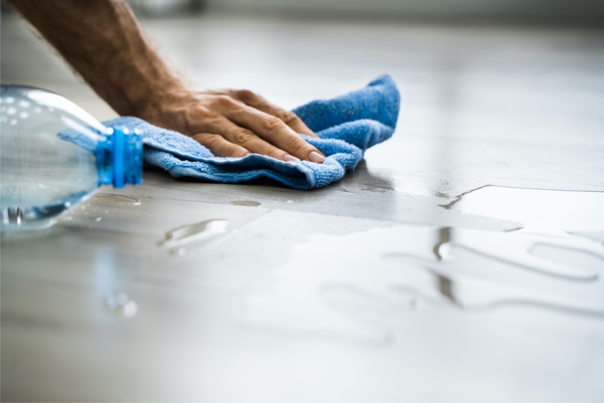 Person wiping spill off a floor with a blue cloth.