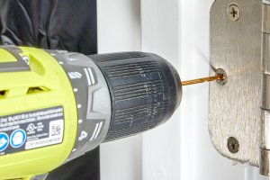 Person drills screw into door hinge.
