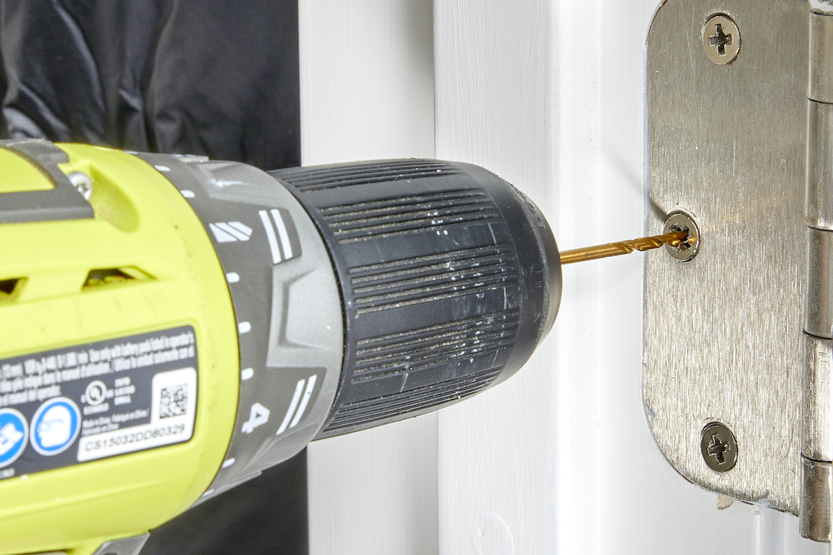 Person drills screw into door hinge.