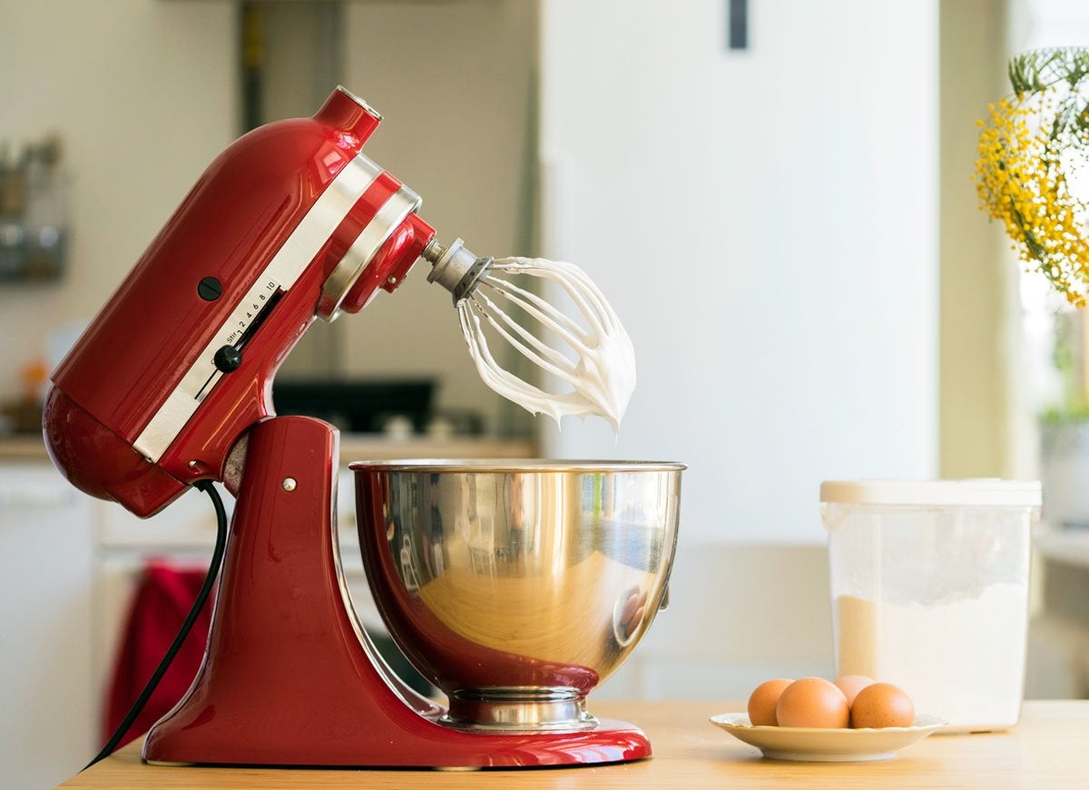Red stand mixer in open position, with whipped egg whites on the beaters.