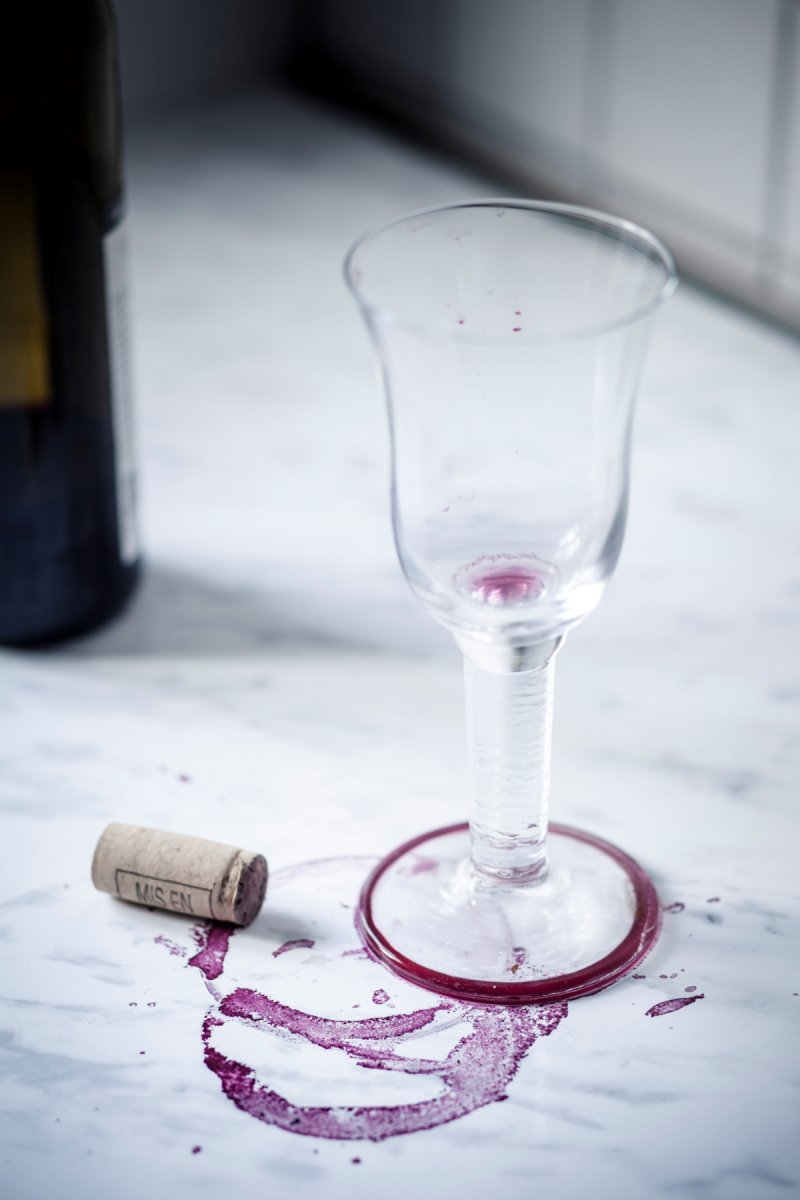 An empty wine glass on a white marble table with red wine stains around the bottom of the glass.