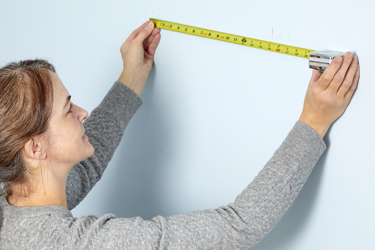 Woman uses a measuring tape to measure a 12-inch span on the wall. 