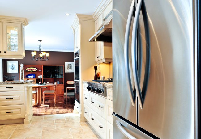 Modern kitchen with light wood cabinets, a stainless steel refrigerator in the foreground.