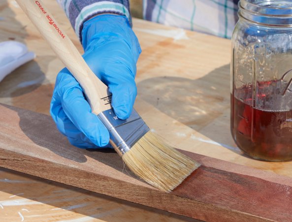 Woman uses a paintbrush to apply Danish oil to a wood board to waterproof it.