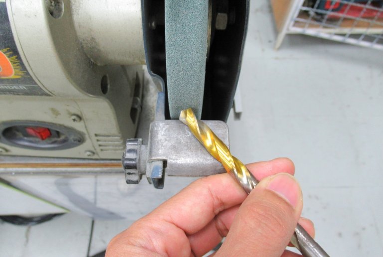 Close up view of person sharpening a drill bit on a bench grinder.