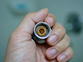 A person is holding a small, circular shower cartridge in their hand.