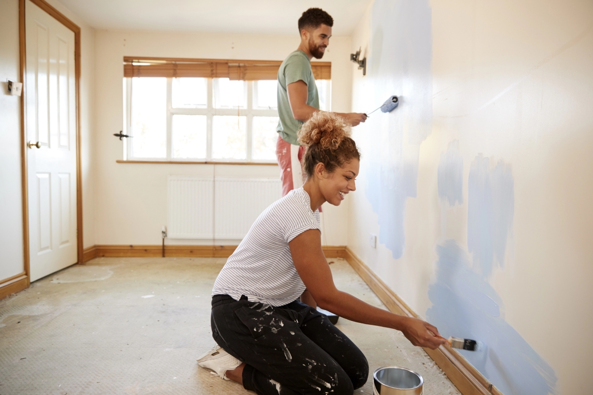 A couple is painting the interior wall of a bedroom.