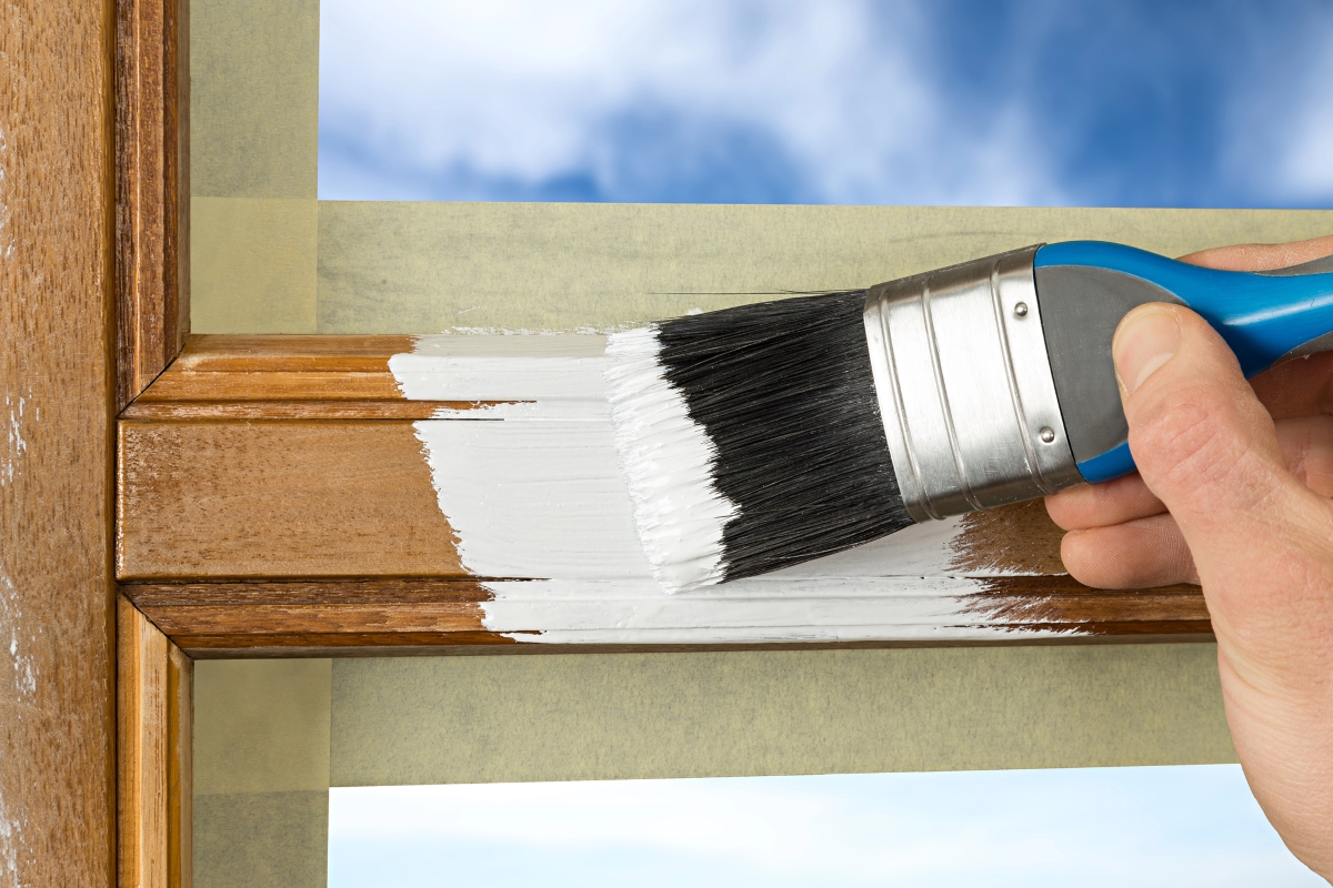 Brush with white paint is used to paint exterior window trim.
