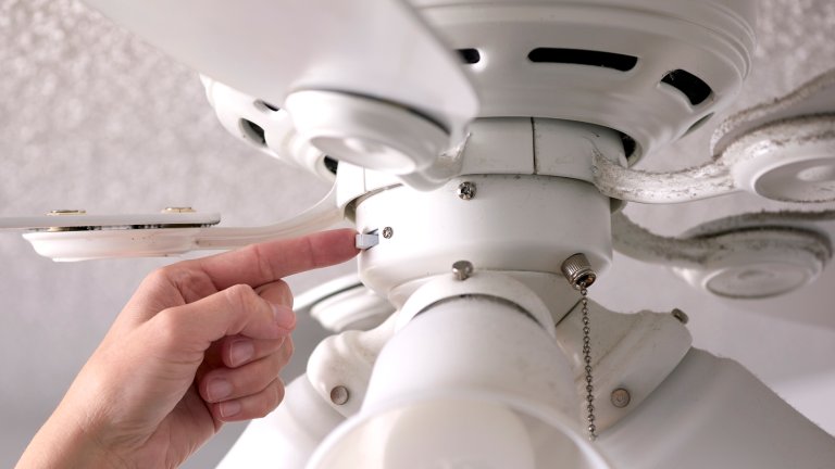 Woman flips a switch on the base of a ceiling fan.