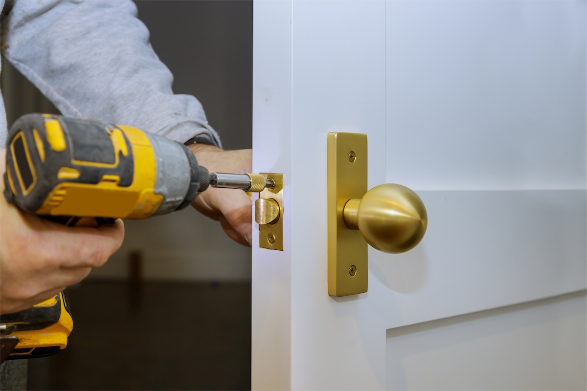 Locksmith uses a screwdriver to install a new lock on a white door.
