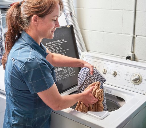 Woman stands in front of front-load washer, distributing laundry evenly inside.