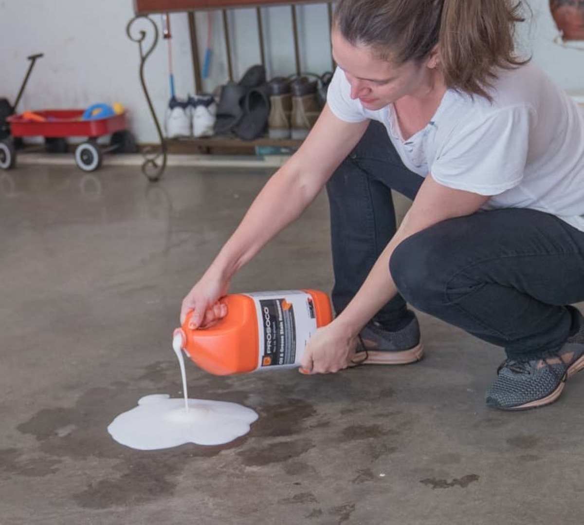 Woman pouring oil and grease stain remover on garage gasoline stain.