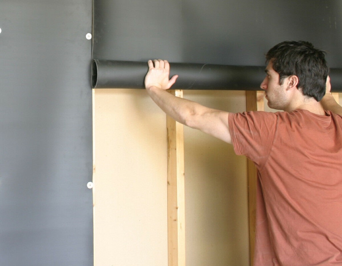 Person installing large roll of mass loaded vinyl sheet on wall.
