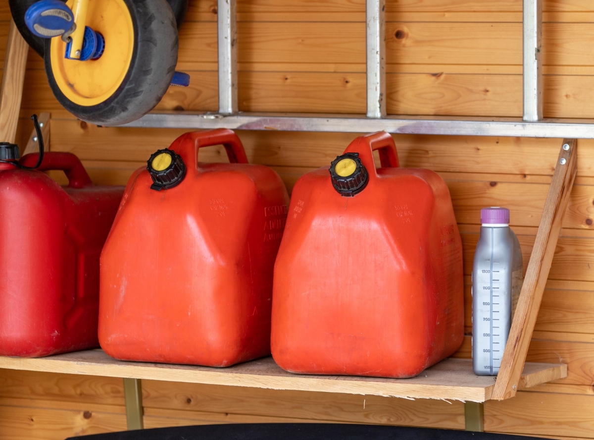 Stored red gasoline containers on wooden shelf.