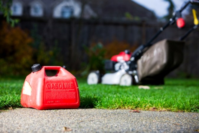 Old red gasoline container with lawnmower in background.