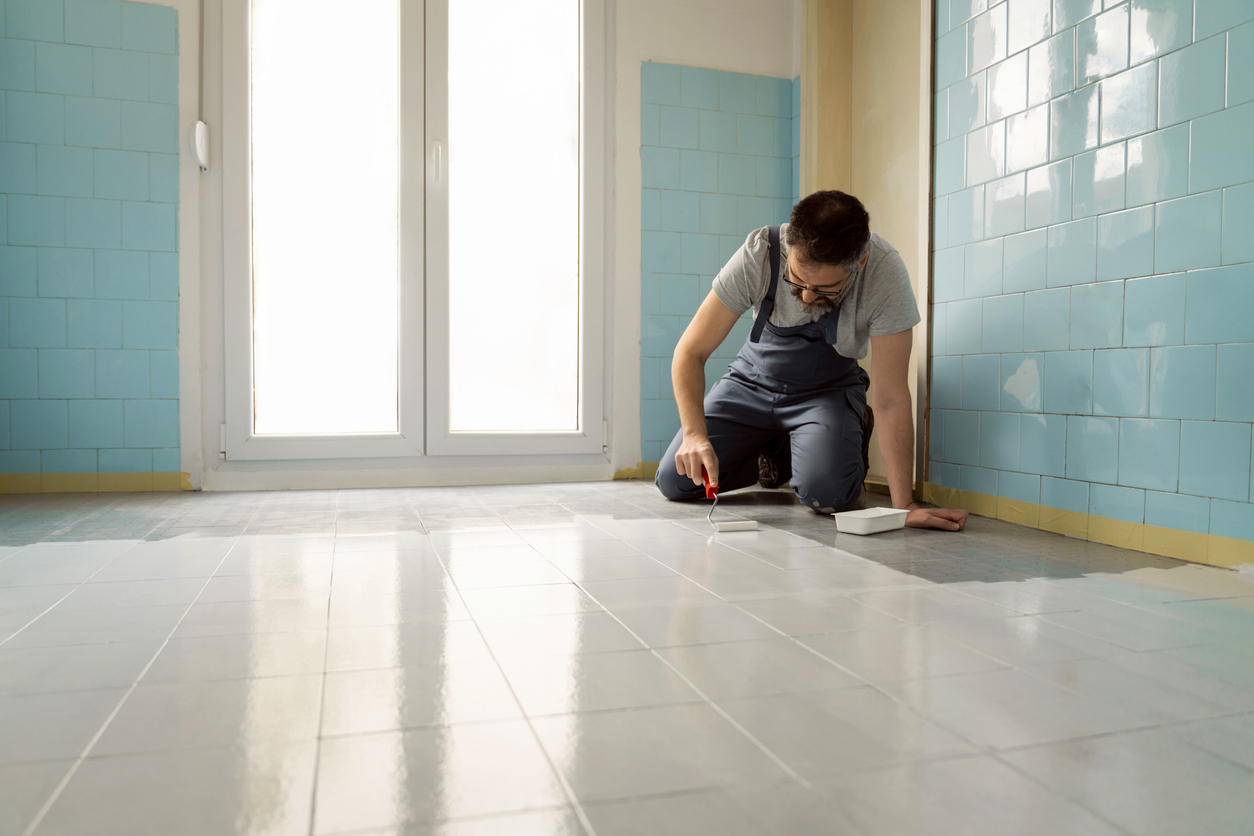 Male Caucasian craft person, painting the floor tiles in the kitchen with white paint