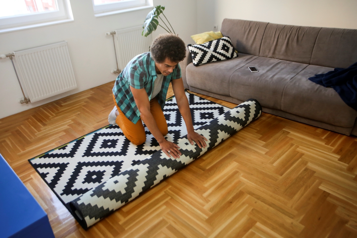 Young man rolling black and white area rug on hardwood floor.