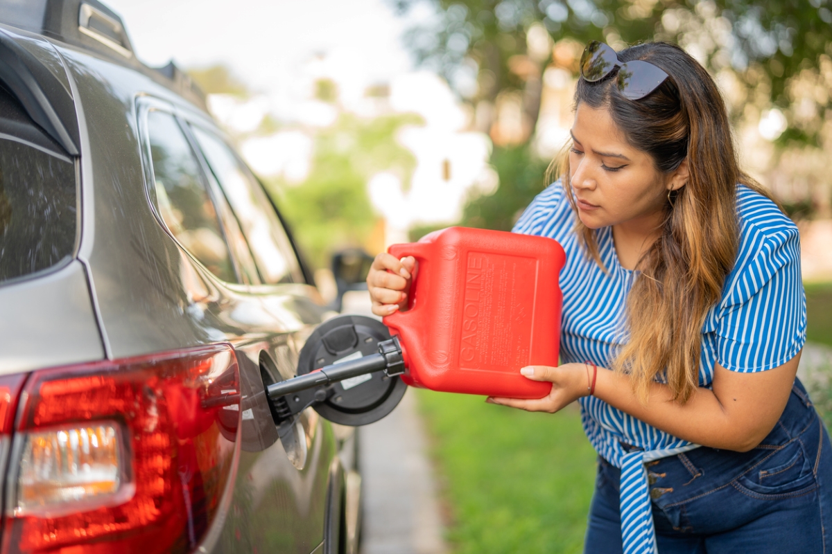 Woman pouring gas from red container in car.