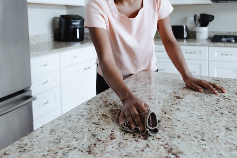 A woman's hands clean the surface of a granite countertop.