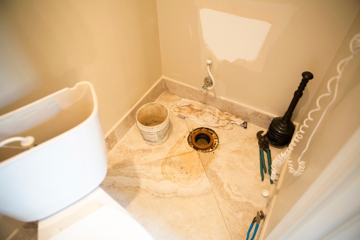 A plumber has taken a toilet apart and disconnected it from the drainpipe on the bathroom. The toilet was leaking at the bottom. The toilet flange connects the toilet to the pipe in the floor.. There is a plunger and pliers on the floor. Taken with Canon 5D Mark 3.