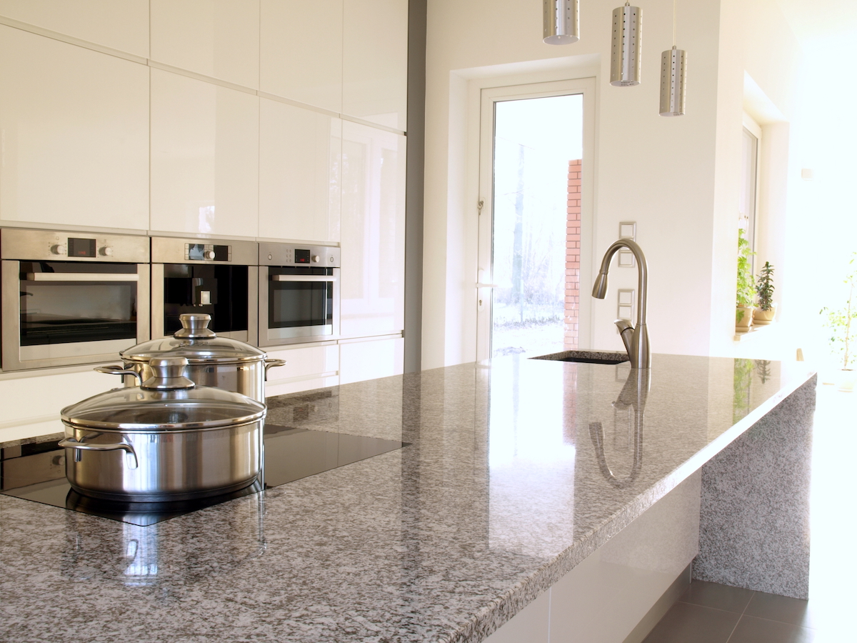 A modern white kitchen with stainless appliances and a grey granite countertop.