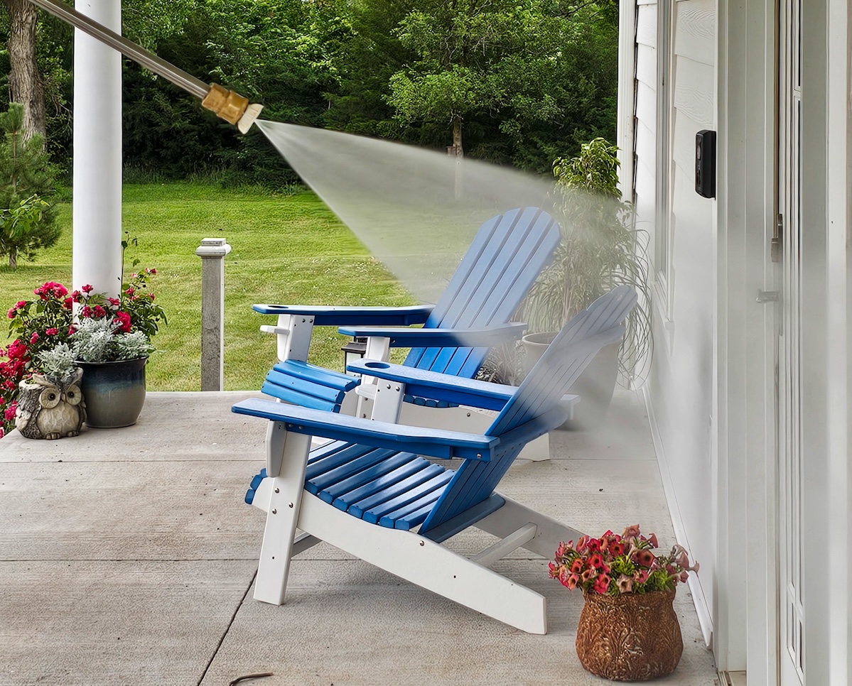 Pressure washer nozzle sprays water on front entry of house with blue outdoor chairs in background.