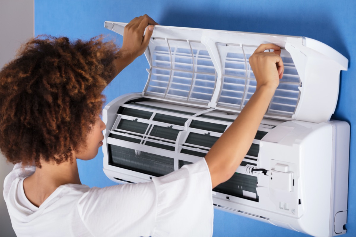Young woman lifts the cover on a mini-split air conditioner to examine the inside.