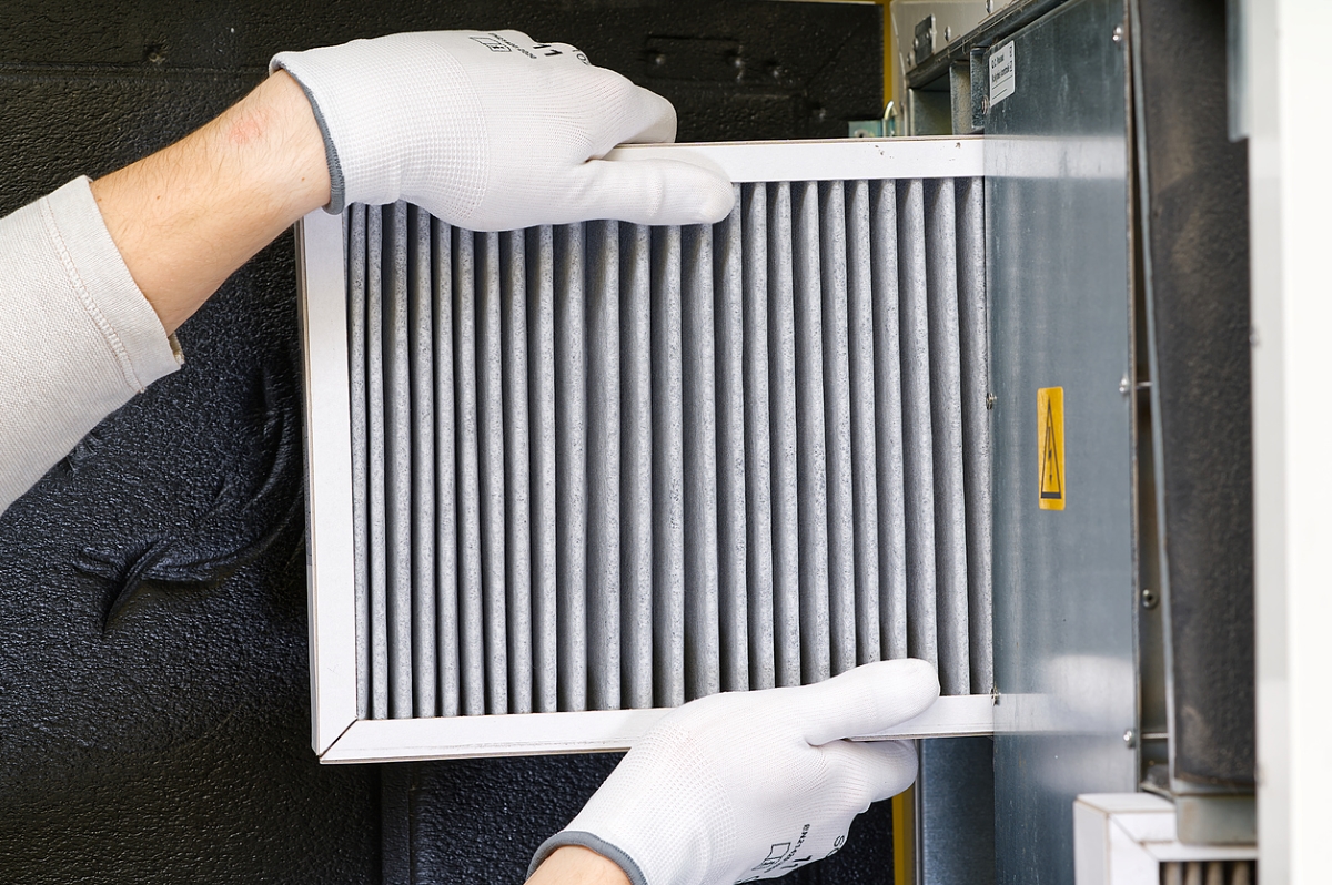 Gloved hands replacing air conditioner filter.