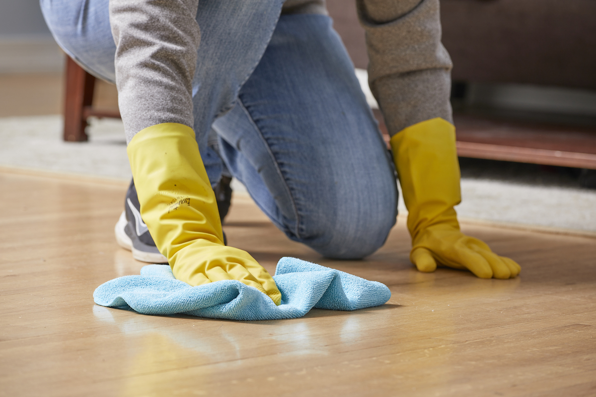 Woman wipes a hardwood floor with a blue microfiber cloth.