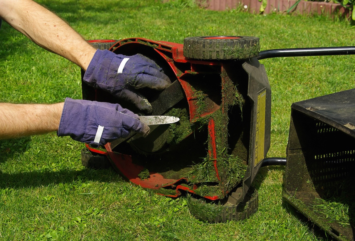 Cutting out blocked grass in lawn mower blades using a small tool. 
