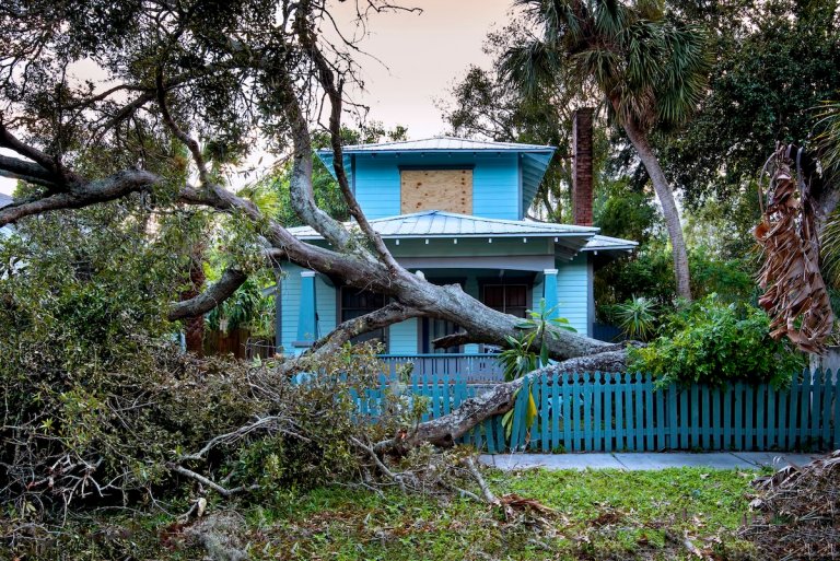 A small blue home with extensive hurricane damage.