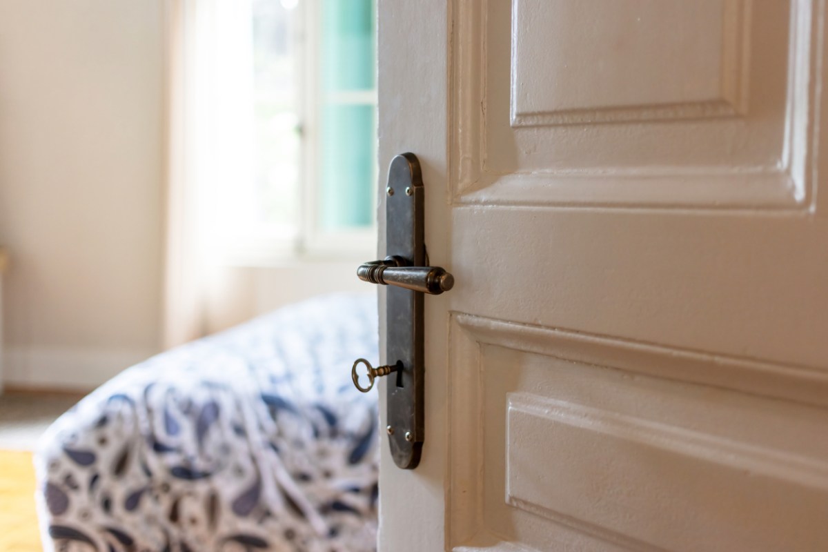 Bedroom door with old-fashioned hardware cracked open to reveal bed duvet.