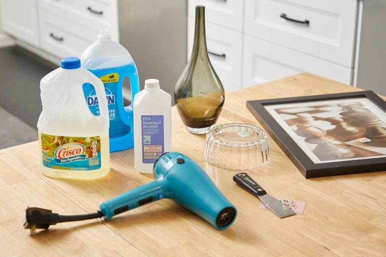 A vase, picture frame, dish soap, oil, hair dryer, and rubbing alcohol on a table.
