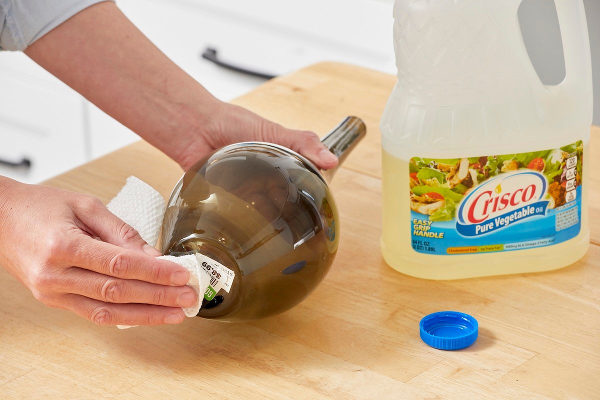 Woman applies cooking oil to a sticker on the bottom of a vase.